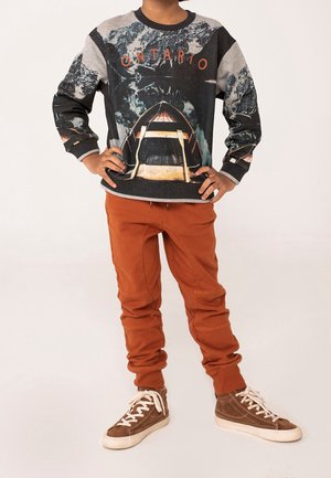 Felpa nera e grigia con grafica di una canoa e la scritta "ONTARIO", abbinata a pantaloni da jogging arancioni e sneaker alte marroni.