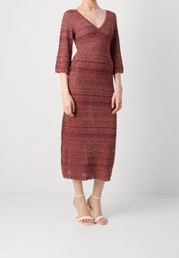 Robe tricotée bordeaux avec un décolleté en V, des manches trois-quarts et une silhouette cintrée. Présente un motif texturé et tombe en dessous du genou.