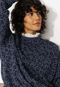 Sweatshirt bleu marine avec un motif de léopard noir, avec un col rond et une texture douce, superposé sur un col en dentelle blanc.