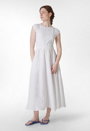 Hvid kjole med korte ærmer, samlet talje, flydende skirt og sidelommer. Båret med blå klipklappere med et enkelt design.
