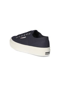 Sneaker in tela blu navy con suola in gomma bianca, punta rotonda, sei occhielli e una piccola etichetta con logo sul lato. Corpo testurizzato con lacci.