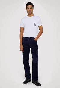 Biała bawełniana koszulka z kieszenią na piersi ozdobioną grafiką; w zestawie granatowe spodnie sztruksowe; czarne obuwie; minimalistyczny design.