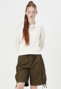 White knitted sweater with open stitch pattern, paired with olive green cargo shorts featuring side pockets and drawstring waist.