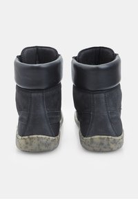 Črne visokotopšne superge z usnjenim manšetom, z nubukovo teksturo in obrabljenim gumijastim podplatom, ki ima piko vzorec.