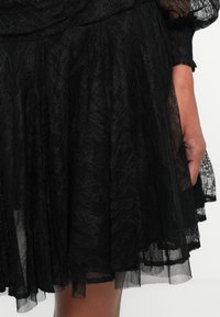 Černá krajková sukně s rozšířeným designem, vrstveným tulle lemem a složitými květinovými vzory. Lehká textura dodává hloubku a pohyb.
