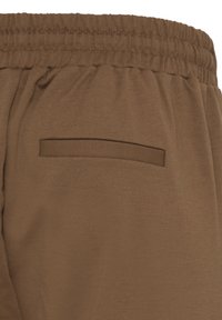 Pantalon à taille élastique marron avec une poche arrière fendue horizontalement, fabriqué en tissu doux et lisse.