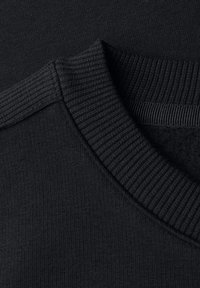 Dettaglio del tessuto di un maglione nero che mostra un colletto a coste e una texture liscia, con un primo piano delle cuciture e della trama del materiale.