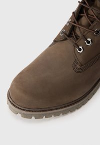 Bottes en cuir marron avec un bout arrondi, des coutures renforcées, des œillets en métal et une semelle en caoutchouc robuste avec un léger motif de traction.