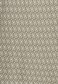 Tecido com padrão geométrico em verde oliva, com formas de diamante brancas e pequenos pontos. Material em algodão com uma textura suave.
