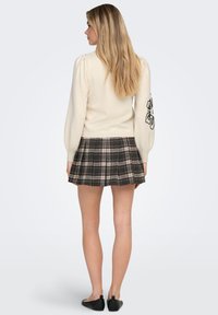 Cremefarvet sweater med puffede ærmer, kombineret med et ternet plisseret nederdel i brune nuancer. Sorte ballerinaer fuldender outfittet.