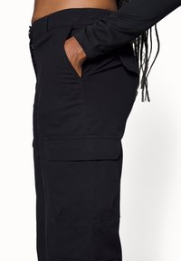 Pantalons cargo noirs en tissu durable, avec des poches latérales, une coupe ajustée et des détails de couture visibles. Le design comprend une taille standard.