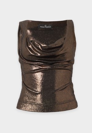Femme aux longs cheveux foncés portant un débardeur noir brillant, un pantalon beige clair à jambes larges et des talons noirs pointus, debout avec une main sur la hanche.