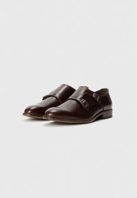 Zapatos de cuero marrón con un acabado suave, que cuentan con dos correas laterales con hebillas de plata, punteras redondeadas y un tacón bajo de madera.