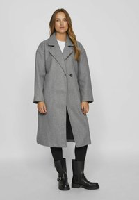 Cappotto in misto lana grigia con colletto a revers, chiusura con un bottone singolo e maniche ampie. Abbinato a stivali neri alla caviglia e leggings.