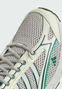 Light grey mesh sneaker with green accents and white overlays. Features textured leather, round laces, and prominent branding on the side.