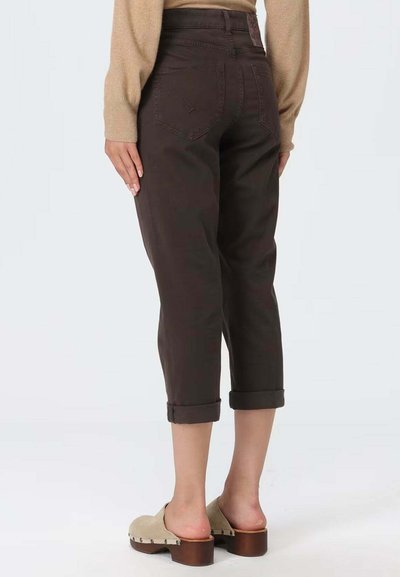 Bruine cropped broek met opgerolde boorden, gemaakt van katoenen stof. Heeft twee achterzakken en een hoge taille. Schoeisel is klompen.