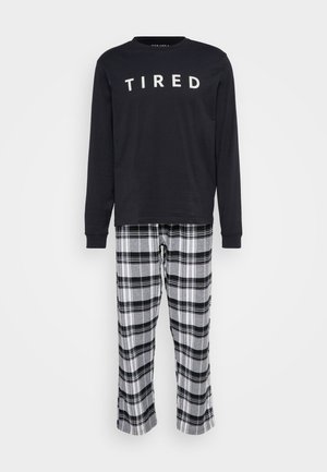 Musta pitkähihaine paita, jossa valkoinen teksti "TIRED", yhdistettynä harmaan ja mustan ruutukuosiset pyjamahousut, joissa on joustava vyötärö ja suorat lahkeet.