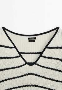 Pull en coton à col en V couleur crème avec des rayures horizontales noires. Présente une texture tricot légère et une bordure noire contrastante au niveau de l'encolure.