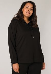 Zwarte hoodie met lange mouwen, gemaakt van een gladde stof. Voorzien van een kangoeroezak en verstelbare koordjes bij de capuchon.