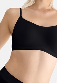 Black bralette with thin straps, smooth texture, and a sleek design. Features a rounded neckline and minimalist style without any embellishments.