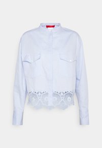 Vaaleansininen lyhytnokkainen paita, jossa on pitkät hihat, napitus, kaksi rintataskua ja koristeellinen pitsireuna kukkakuviolla.