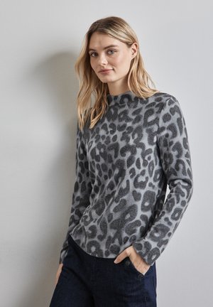 Pull en tricot gris avec imprimé léopard noir, col montant et manches longues. Texture douce, associé à un jean foncé avec détail de boutons.