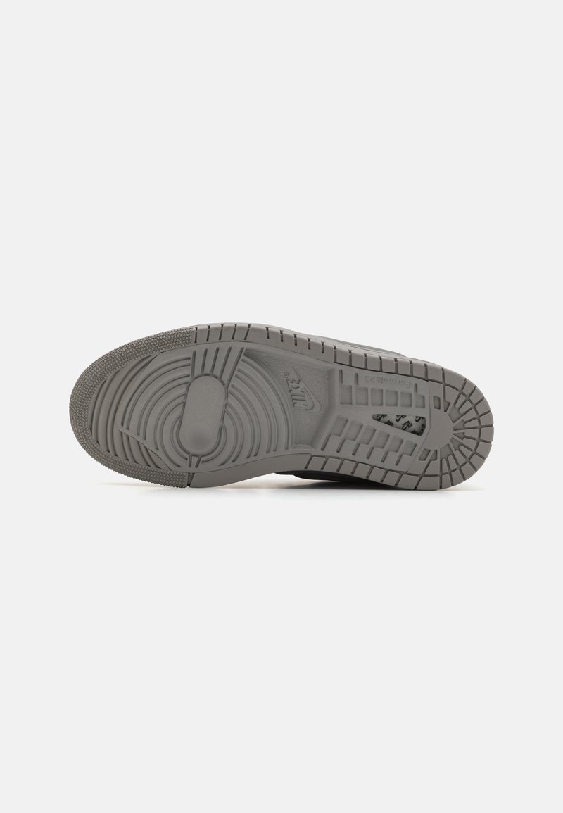 Suela de zapatilla gris con un patrón de goma texturizada que presenta diseños circulares y lineales. Incluye un logo y surcos distintivos para mejorar la tracción.