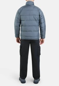 Giacca imbottita grigia con colletto alto e trapuntatura orizzontale, abbinata a pantaloni cargo neri con tasche laterali. Materiale testurizzato e resistente.