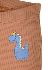 Beige geripptes Gewebe mit einem blauen Dinosaurier-Applikation, der einen gekrönten Kopf und ein gepunktetes Design hat. Die Nähdetails betonen die Textur.