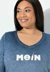 Niebieski T-shirt z dekoltem w serek, wykonany z miękkiej tkaniny, z dużym napisem "MOIN" w białych literach oraz grafiką kotwicy i butelki.