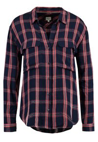 Navy blue long-sleeve shirt with red and white plaid pattern. Features two chest pockets, button front, and a curved hem. Soft fabric texture.