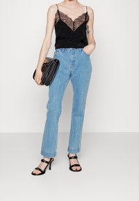 Černá saténová košilka s krajkovým lemem, světle modré džíny s vysokým pasem a černé sandály na podpatku. Drží černou kabelku se zlatými akcenty.