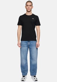 T-shirt nera in cotone con maniche corte e scollatura rotonda, abbinata a jeans in denim blu chiaro. Le calzature presentano accenti in bianco e nero.