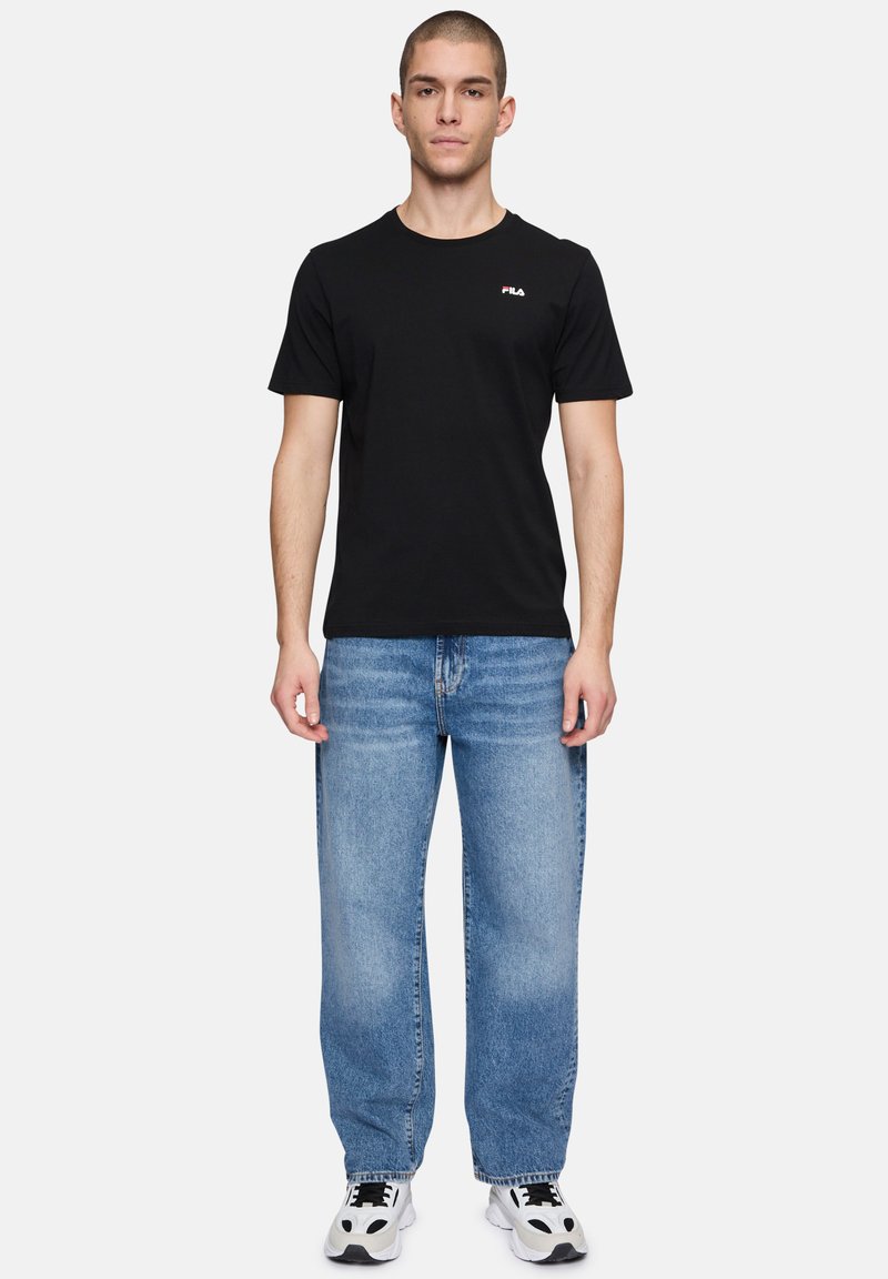 T-shirt nera in cotone con maniche corte e scollatura rotonda, abbinata a jeans in denim blu chiaro. Le calzature presentano accenti in bianco e nero.