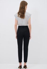 White blouse with black polka dots and flutter sleeves, paired with high-waisted black tailored trousers. Smooth textures, fitted silhouette.
