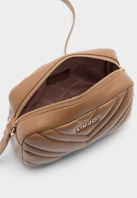 Brązowa, pikowana skórzana torebka crossbody z górnym zamkiem błyskawicznym, złotymi akcentami i wnętrzem z podszewką w wzór logo.