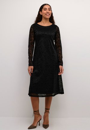 Robe en dentelle noire avec de longues manches transparentes, décolleté rond, motif floral complexe, mi-longue et une silhouette légèrement évasée.