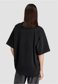 Črna oversized majica s kratkimi rokavi in sproščenim krojem. Narejena iz gladke bombažne tkanine, z okroglim izrezom.