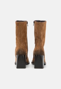 Bottines en daim marron avec un talon carré, dotées d'une fermeture éclair et de coutures sur les côtés. Doublure intérieure lisse.