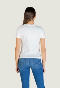 T-shirt bianca a maniche corte con scollo rotondo, abbinata a jeans di denim blu con tasche posteriori. Tessuto di cotone liscio, design aderente.