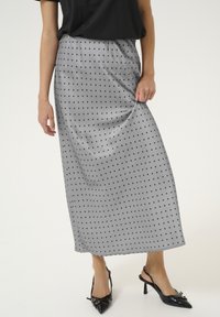 Falda de satén gris con lunares negros, de longitud media, con textura suave y cinturilla elástica, combinada con tacones slingback negros.