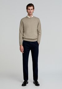 Beige gebreid sweater met ronde hals, gecombineerd met donkere marineblauwe broek. Zwarte schoenen maken de outfit af. Eenvoudig ontwerp, zonder zichtbare patronen.