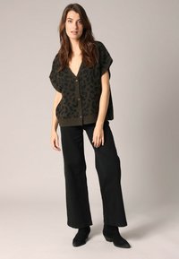 Cardigan imprimé léopard kaki avec un col en V, des manches courtes et des boutons marron, associé à un pantalon noir large et des bottines.