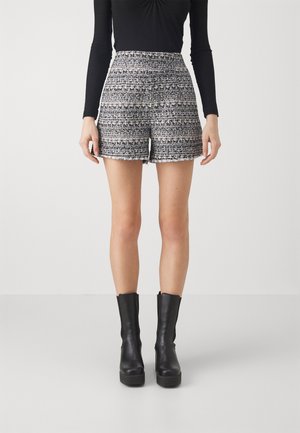 Vrouw draagt een zwarte, witte en grijze tweed korte broek met hoge taille, gecombineerd met een zwart top met lange mouwen en zwarte enkellaarsjes.
