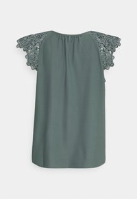 Blouse vert sauge à encolure froncée et manches courtes en dentelle à motif floral, vue de dos sur fond uni.