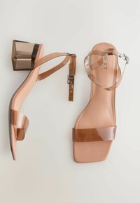 Nude klackade sandaler med en genomskinlig plastöverdel, en tjock genomskinlig klack och ett ankelsnöre. Slät textur och minimalistisk design.