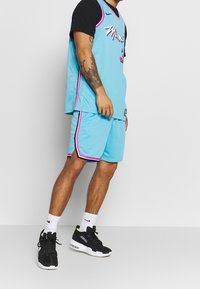 Ensemble de maillot de sport et de shorts bleu clair avec des accents noirs, des bordures roses, et "Miami" imprimé sur le maillot. Porté avec des baskets noires et des chaussettes blanches.