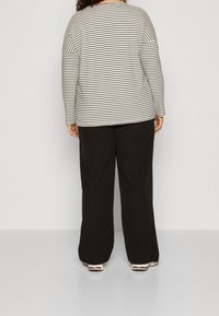 Long-sleeve striped top in cream and black, paired with loose black pants. The top features a round neckline and contrasting sleeve design.