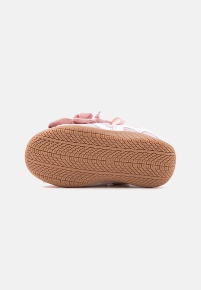 Vue de la semelle d'une basket rose pour enfant avec un motif de crampons texturé et une tige en tissu visible de l'arrière.