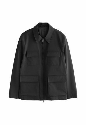 Musta vetoketjullinen takki, jossa on neljä suurta läppätaskua, pitkät hihat ja kärjellisellä kauluksella varustettu malli, esillä valkoisella taustalla.